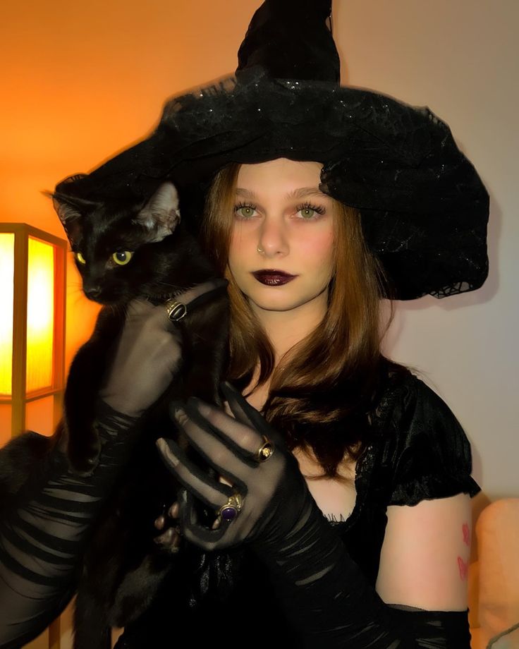 a woman in a witch costume holding a black cat