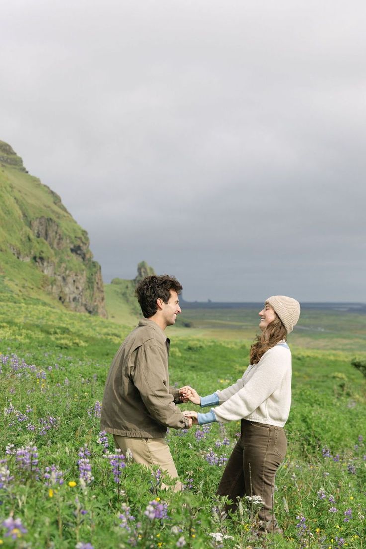 a man and woman holding hands in a field with wildflowers on the hillside