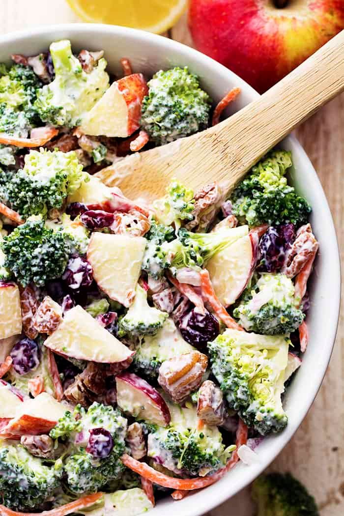 a bowl filled with broccoli, apples and cranberries next to an orange