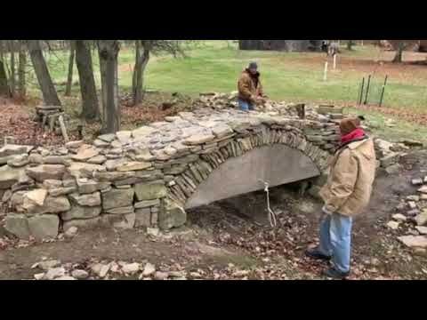 two people are standing near a stone bridge