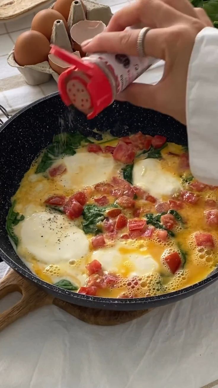 someone is cooking eggs and spinach in a skillet on a table with utensils