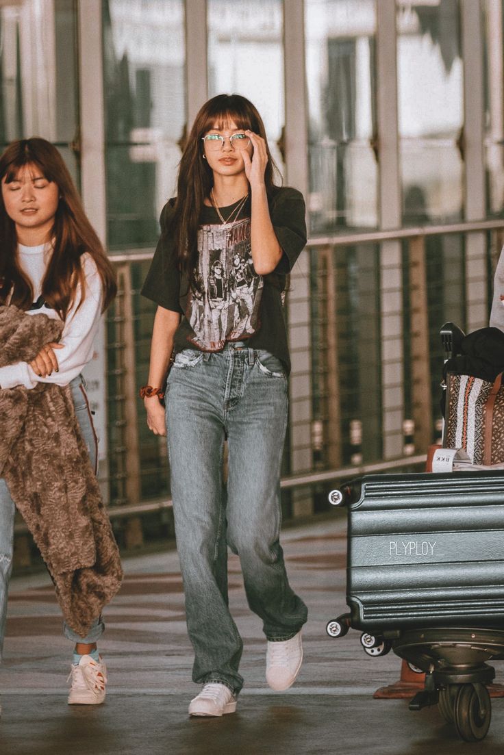 two young women walking down the street with their luggage and one is talking on her cell phone