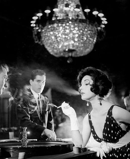 a woman sitting at a bar with two men and a chandelier in the background