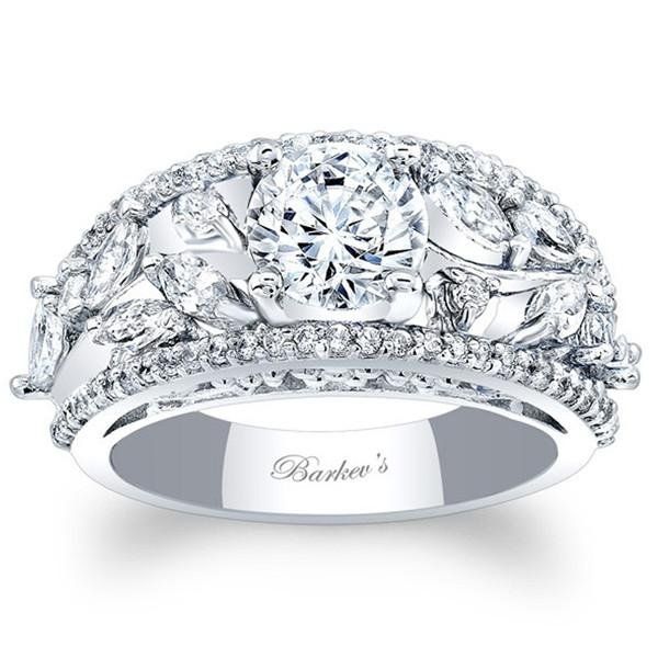 a white gold engagement ring with diamonds on the band and an oval center stone surrounded by leaves