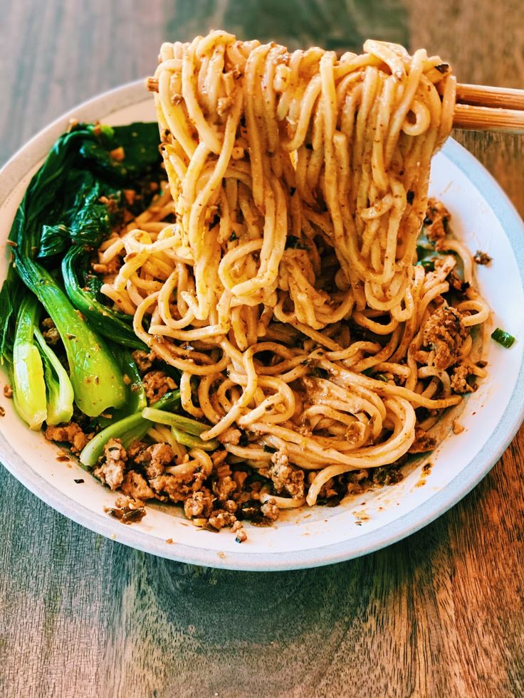 noodles and vegetables on a plate with chopsticks in the middle, ready to be eaten