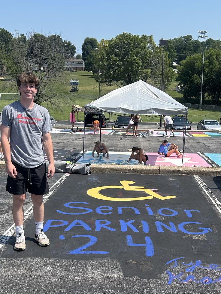 a man standing in front of a parking lot with chalk writing on the ground and people laying around