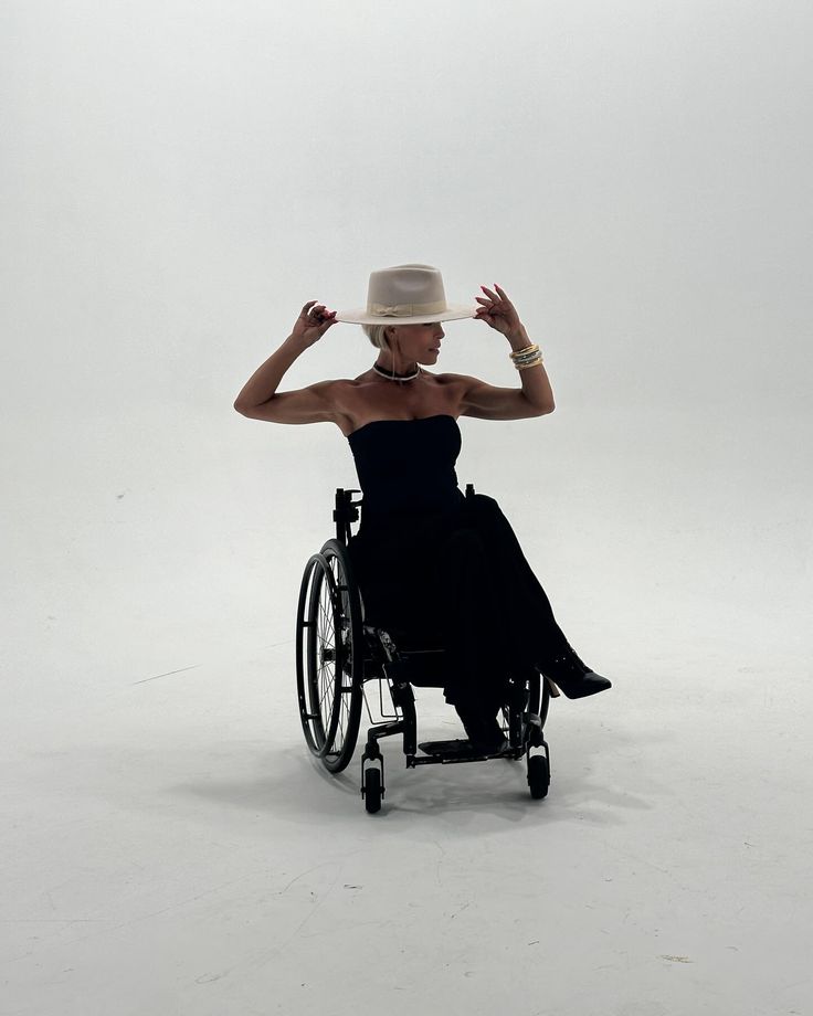 a woman in a wheel chair with a hat on her head and hands behind her head