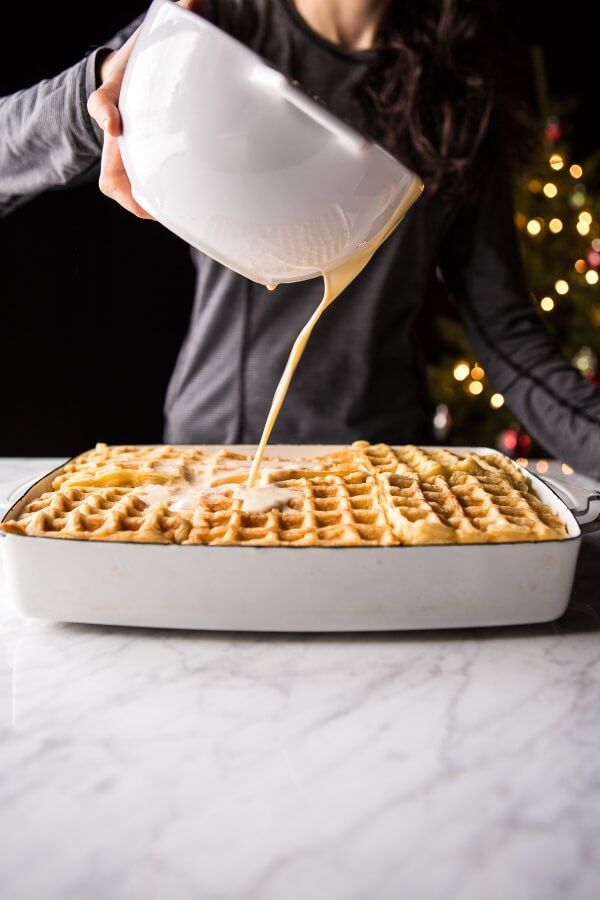 a woman pours syrup over a waffle on top of a white plate with a christmas tree in the background