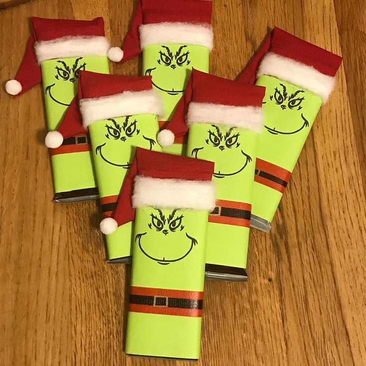 six green wrapped presents with santa hats and grin face drawn on them sitting on a wooden table