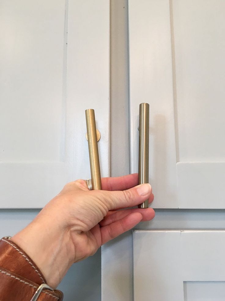 a person is holding two brass cylinders in front of a white door with wood handles