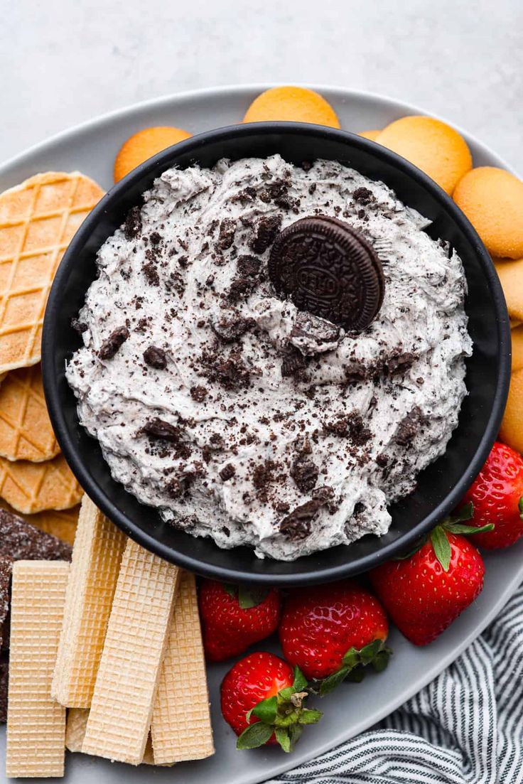 a plate with cookies and cream dip surrounded by crackers, strawberries and oranges