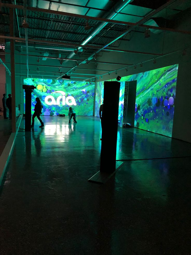 people are walking in an empty building with green and blue lights on the wall behind them