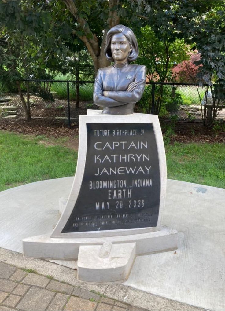 a statue of a woman with her arms crossed next to a sign that reads captain kalthyn janeway