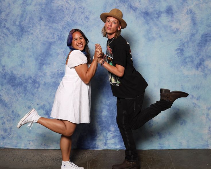 two people standing next to each other in front of a blue background holding hands and dancing