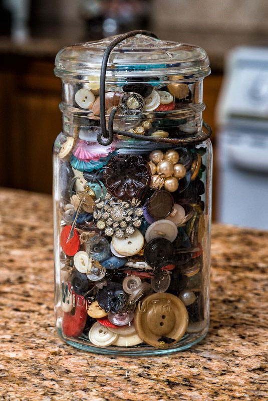 a glass jar filled with lots of different types of buttons on top of a counter