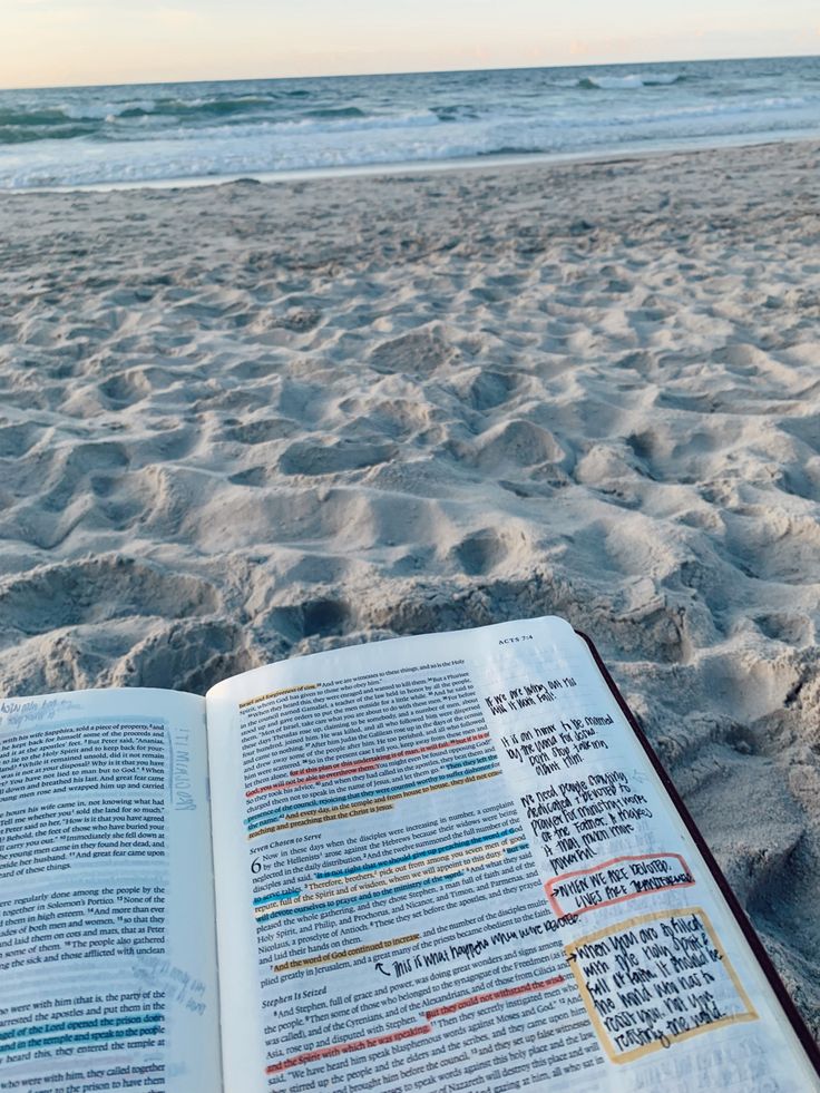 an open book sitting on top of a sandy beach