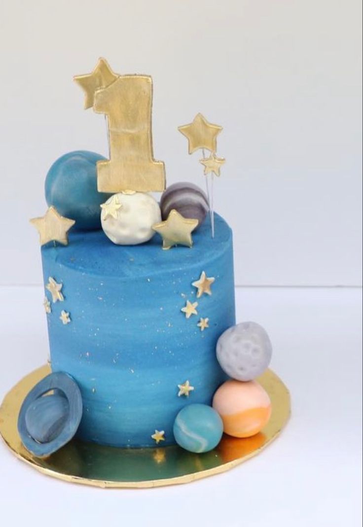 a blue birthday cake with stars and planets on the top is decorated with gold, silver, and blue icing