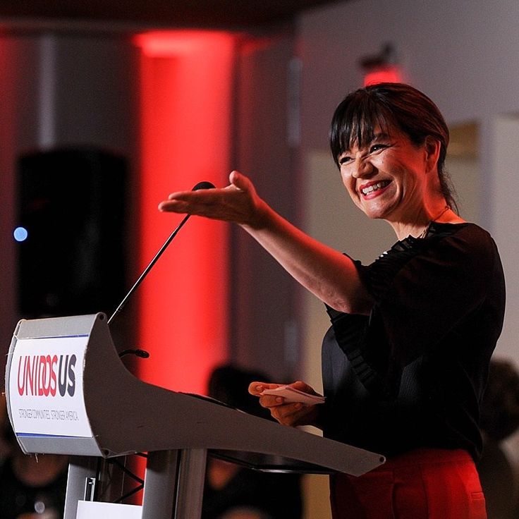 a woman standing at a podium with her hand out and giving a speech to people