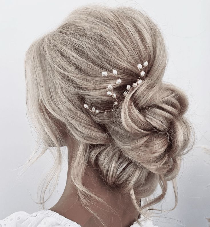 a woman with blonde hair in a low bun and some pearls on her head is shown from the back