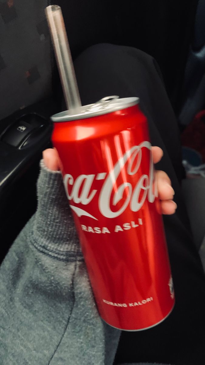 a person holding up a coca - cola can in the back seat of a car