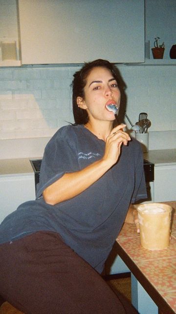 a woman brushing her teeth while sitting at a table with a cup in front of her