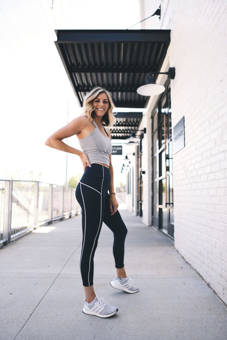 a woman is standing on the sidewalk in her sports bra and leggings, smiling at the camera