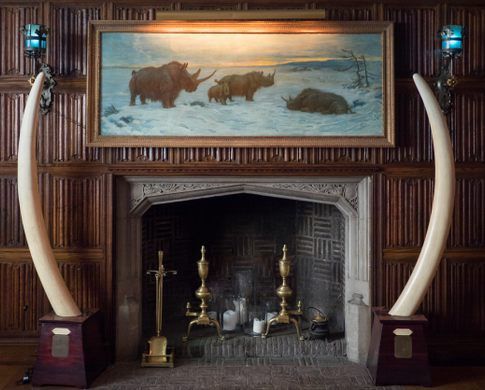 a painting on the wall above a fireplace in a room with wooden paneling and walls