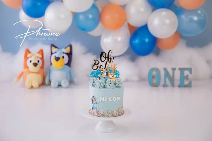 a blue and white birthday cake sitting on top of a table next to some balloons