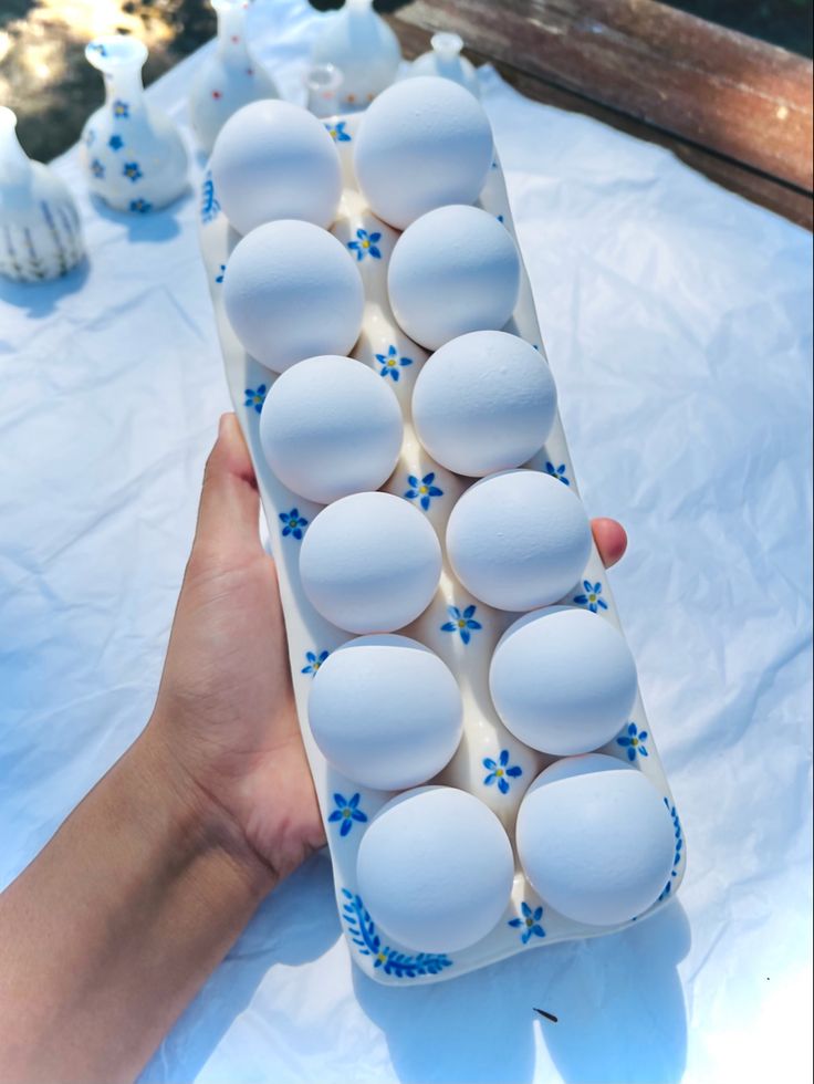 a person holding an egg carton full of white eggs on a blue and white table cloth