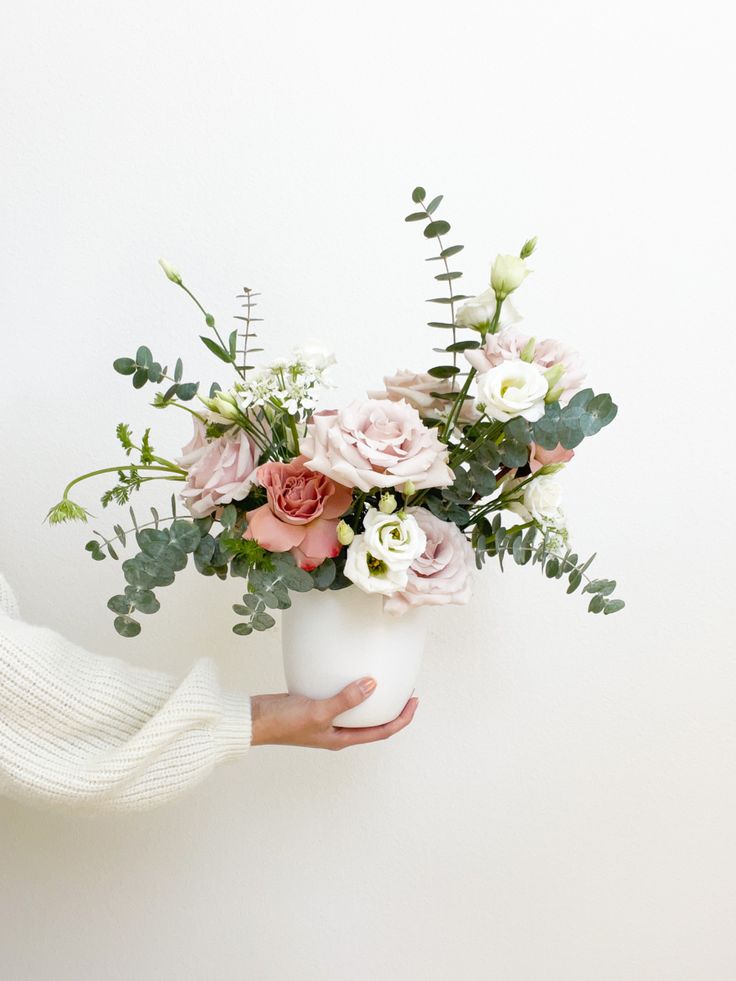 a person holding a white vase filled with flowers