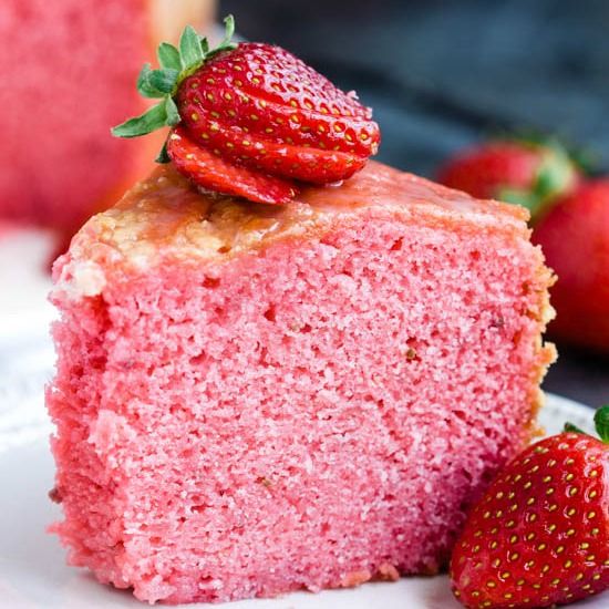 a piece of strawberry cake with two strawberries on the top and one slice missing