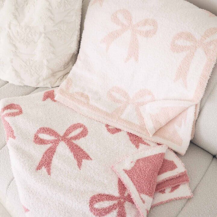 two pink and white towels on a couch next to each other with bows on them