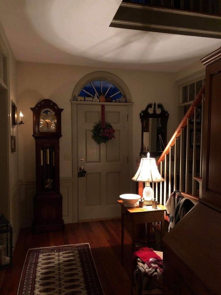 an entry way with a clock and lamp on the table in front of the door