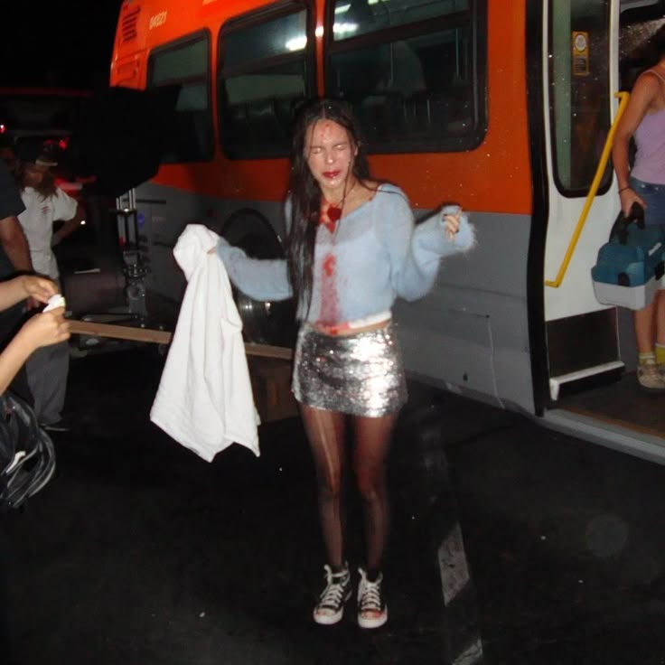 a woman standing in front of a bus with blood all over her face and arms