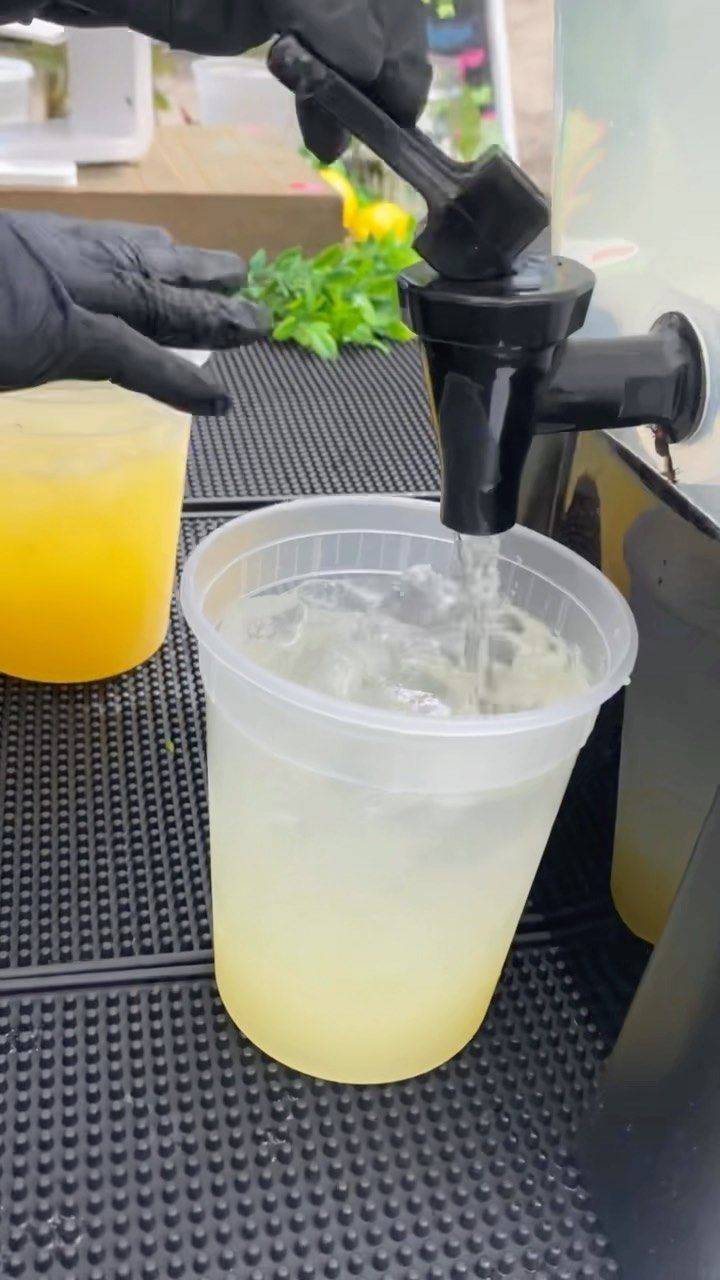 a person in black gloves is pouring something into a plastic cup with a yellow liquid