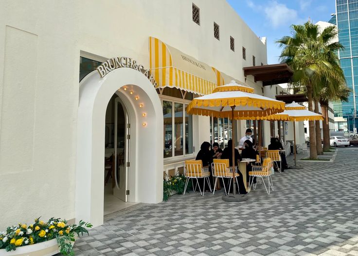 people are sitting at tables under umbrellas on the sidewalk in front of a building