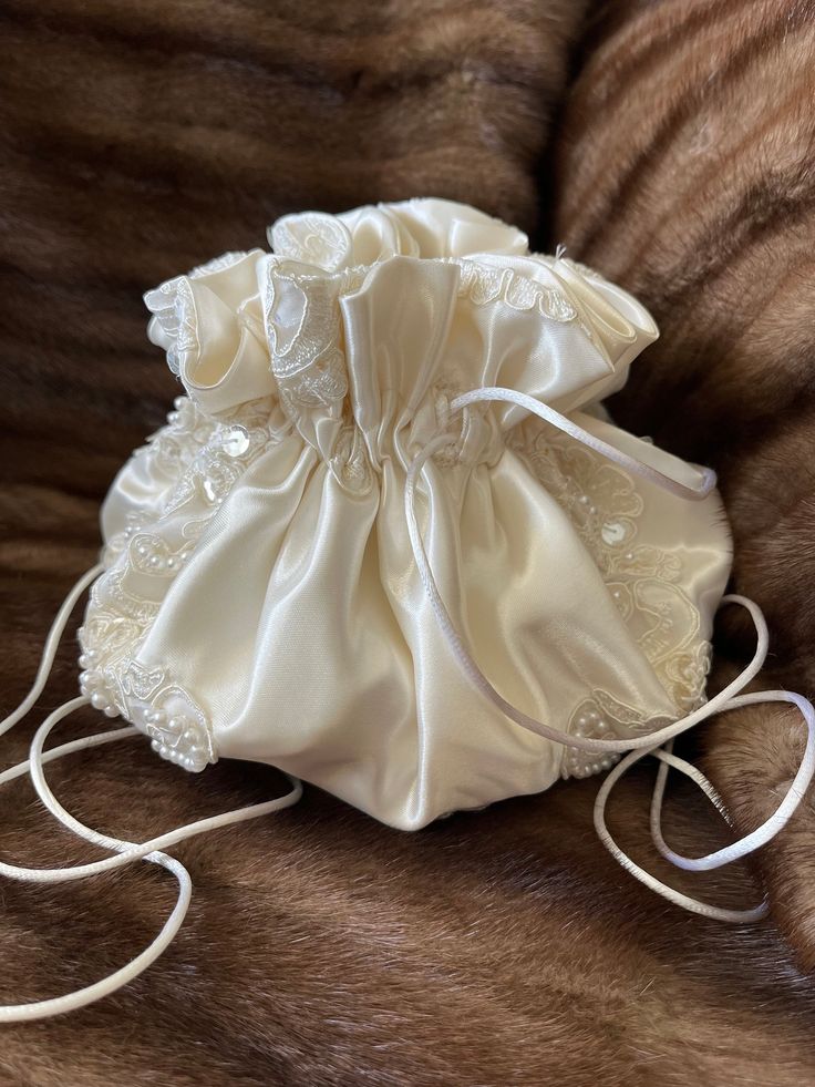 a white satin bag sitting on top of a fur covered bed next to a brown pillow