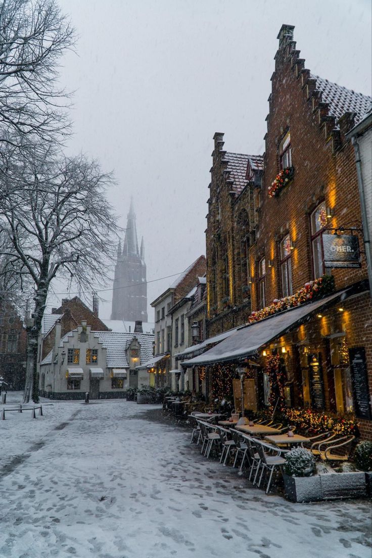 a snowy street lined with buildings and tables in front of a tall church steeple