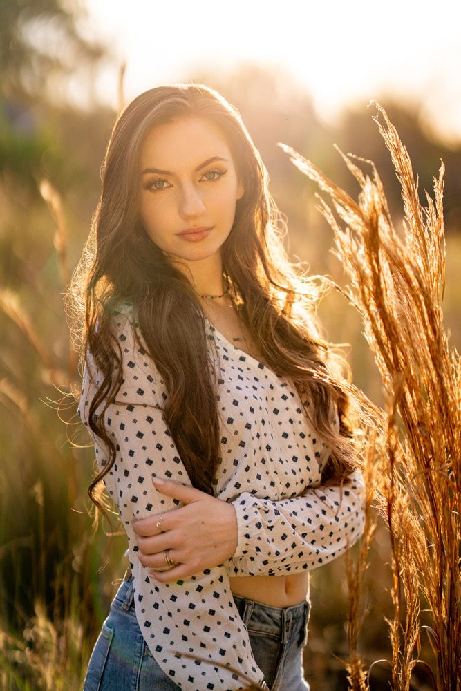 a beautiful young woman standing in a field with her arms crossed and looking at the camera