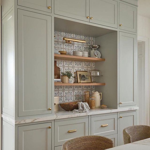 a kitchen with gray cabinets and white counter tops, gold pulls on the cupboards