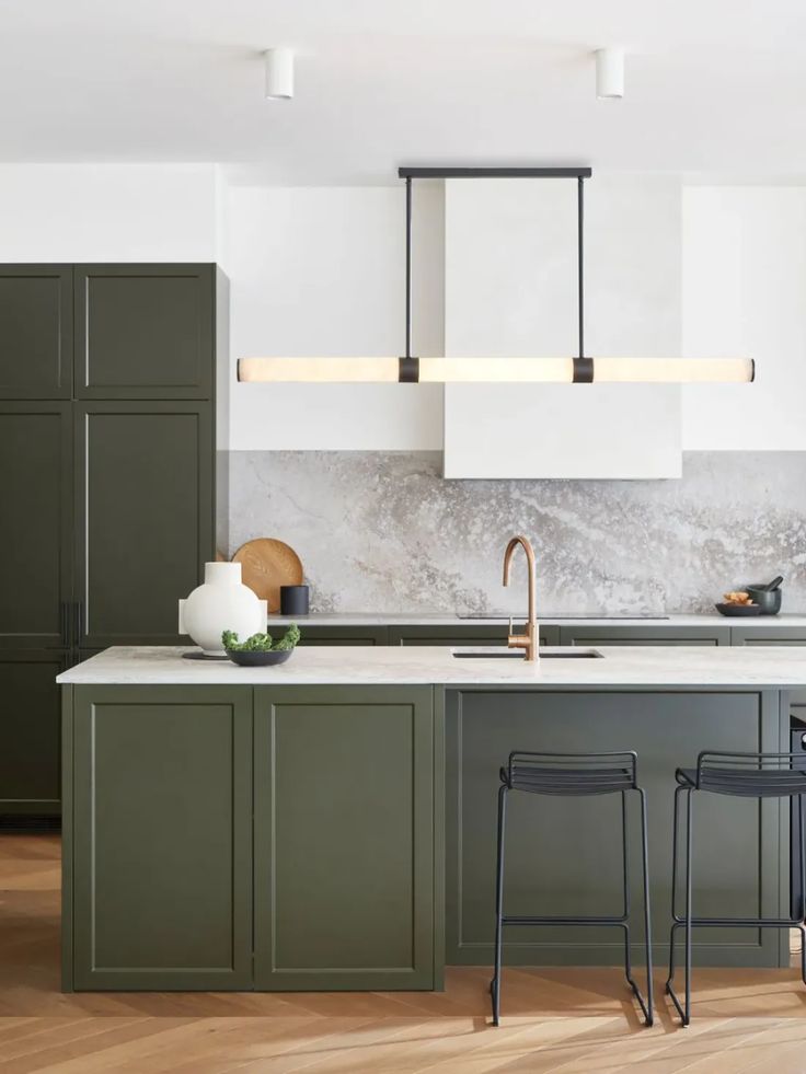 an image of a kitchen setting with green cabinets and marble counter tops on the island