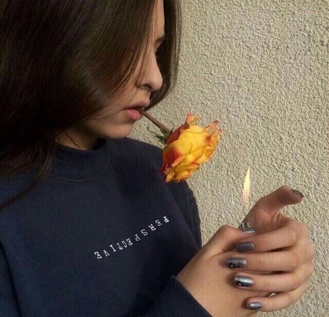 a woman holding a yellow rose in her right hand and looking down at the ground