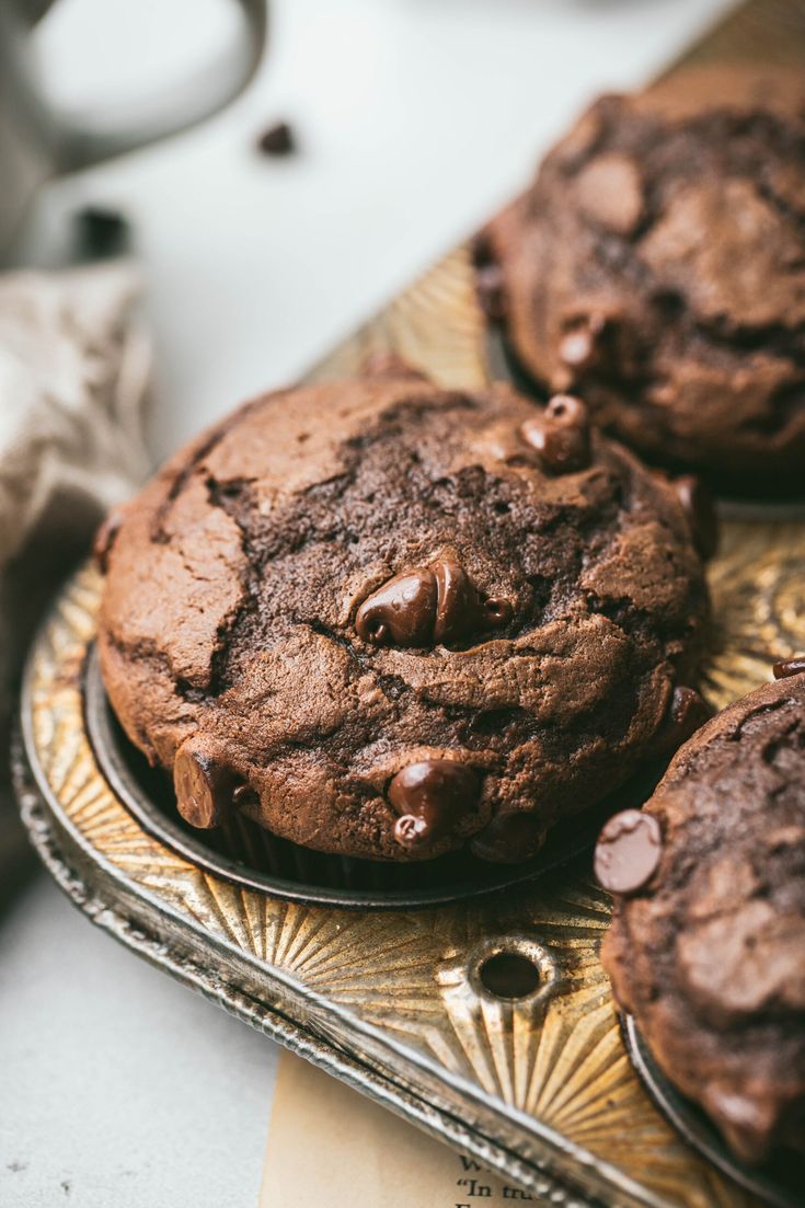 three chocolate cookies sitting on top of a metal tray next to a cup of coffee