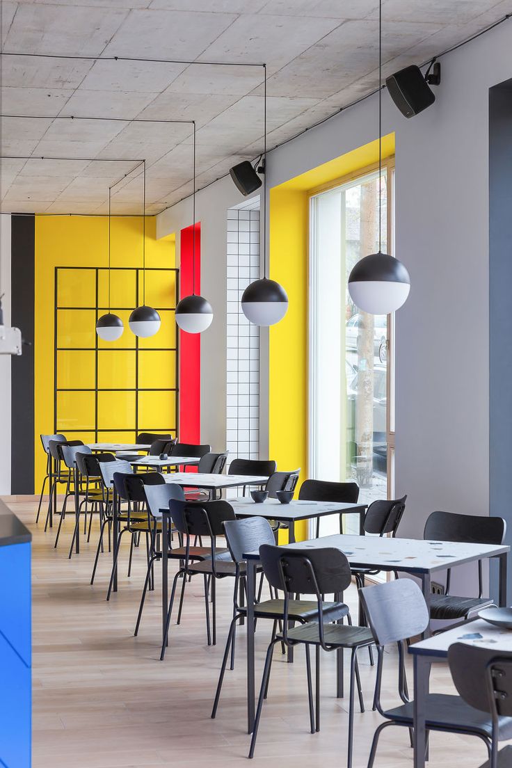 an empty restaurant with tables and chairs in front of bright colored walls, along with hanging lights