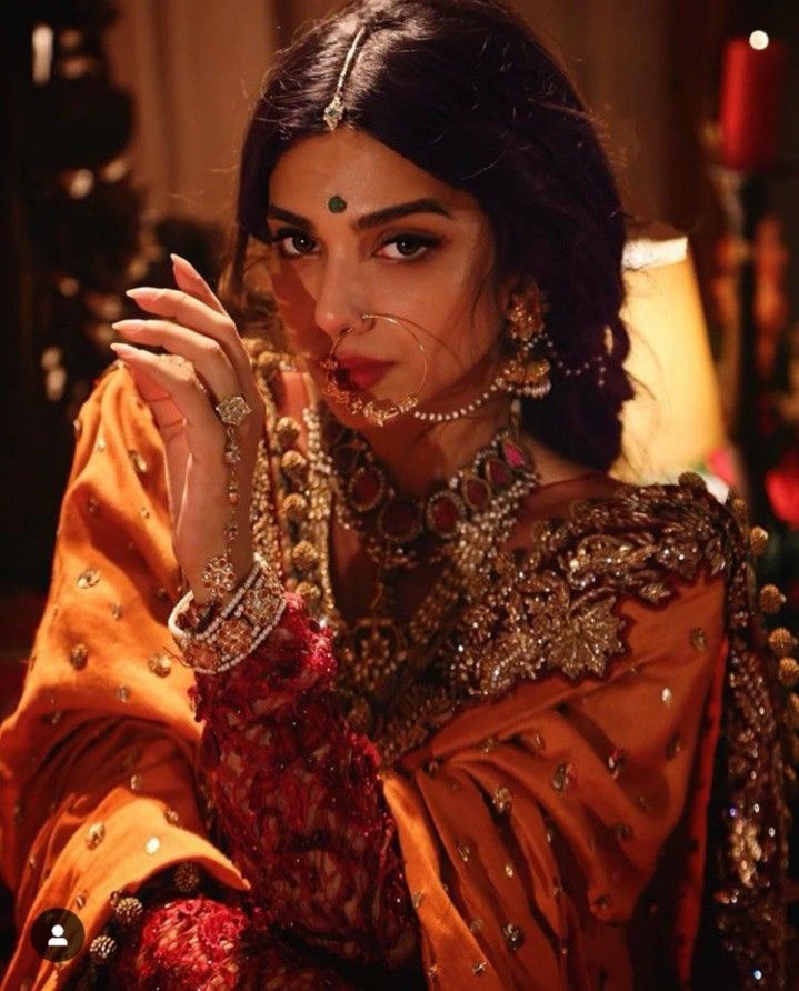 a woman in an orange outfit with jewelry on her head and hands near her face