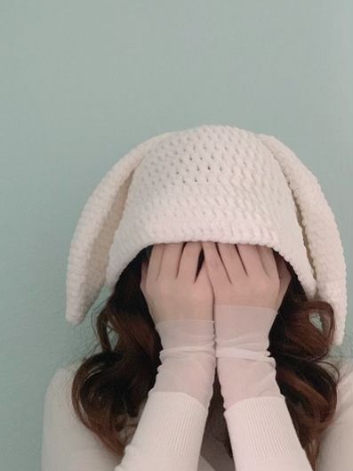 a woman covering her face with both hands while wearing a white knitted hat and gloves