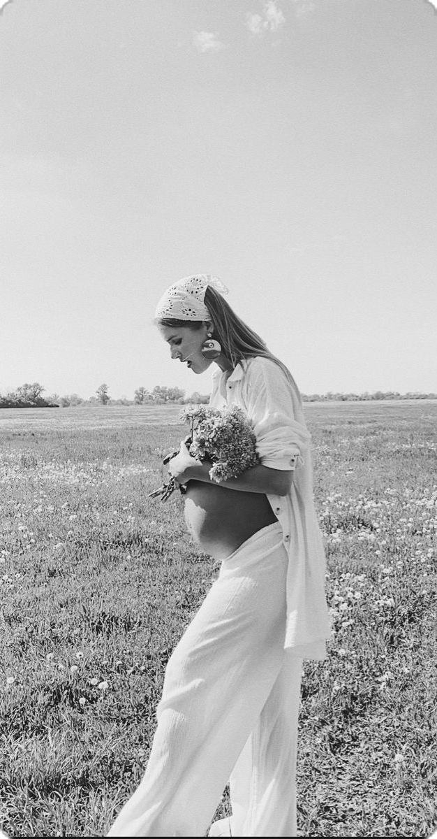 black and white photograph of a pregnant woman in a field with flowers on her belly