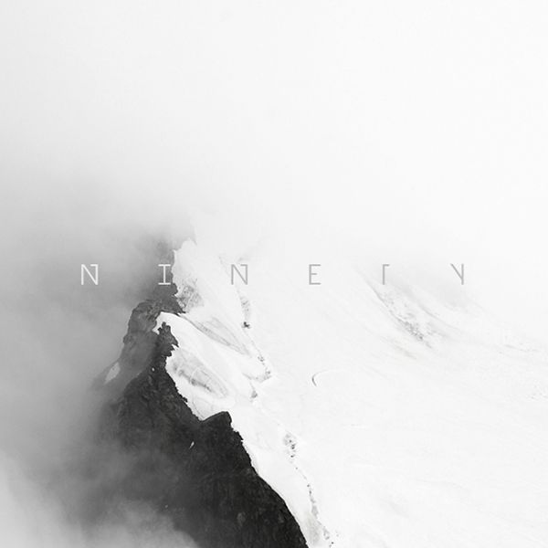 black and white photo of snow covered mountain peak with fog in the foreground, taken from below