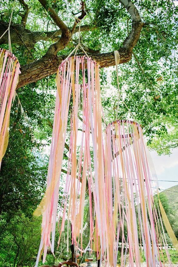 pink and yellow streamers hanging from a tree in the woods for an outdoor ceremony