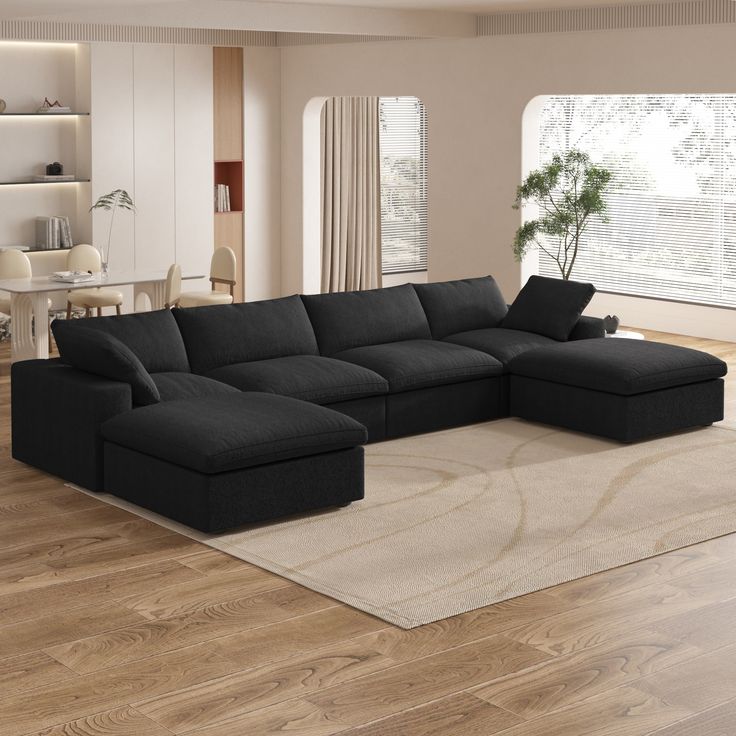 a large black sectional sofa in a living room with hardwood floors and white walls, along with a rug on the floor